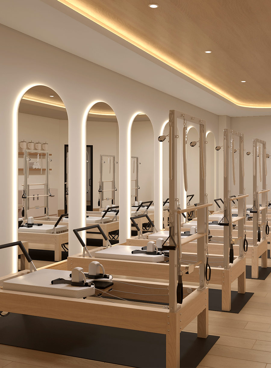 Empty pilates studio with reformers and back lit rounded mirrors under soft lighting