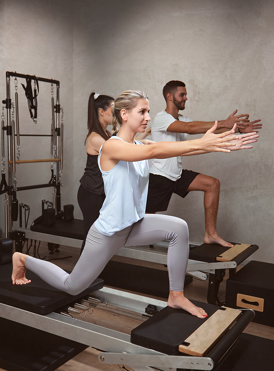 young woman and man exercising in a gym with personal trainer on pilates machine